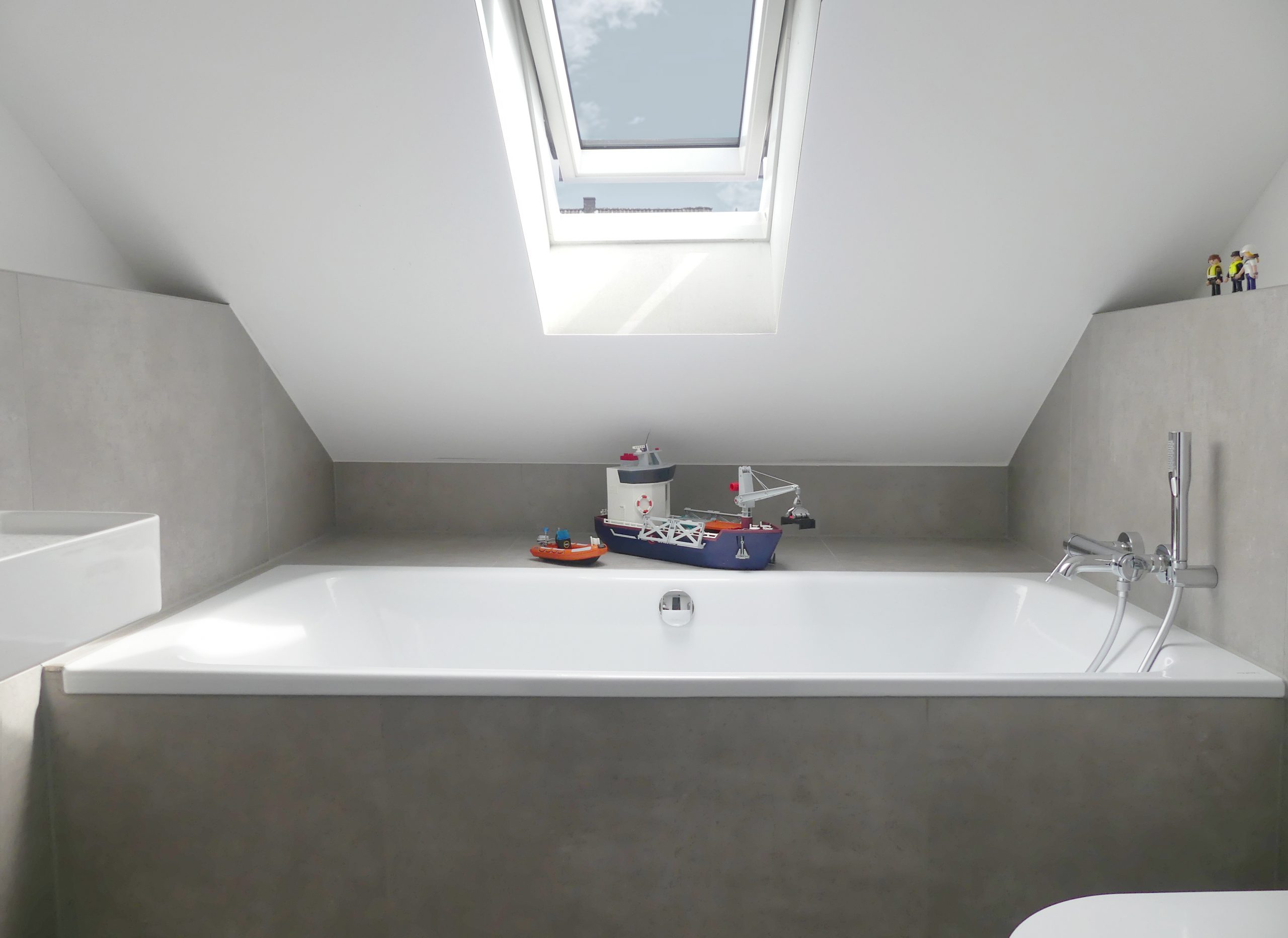 Neues Bad im Dachboden mit Badewanne unter dem Dachfenster und einem Bereich für Kinder zum Spielen – modernes Badezimmerdesign.