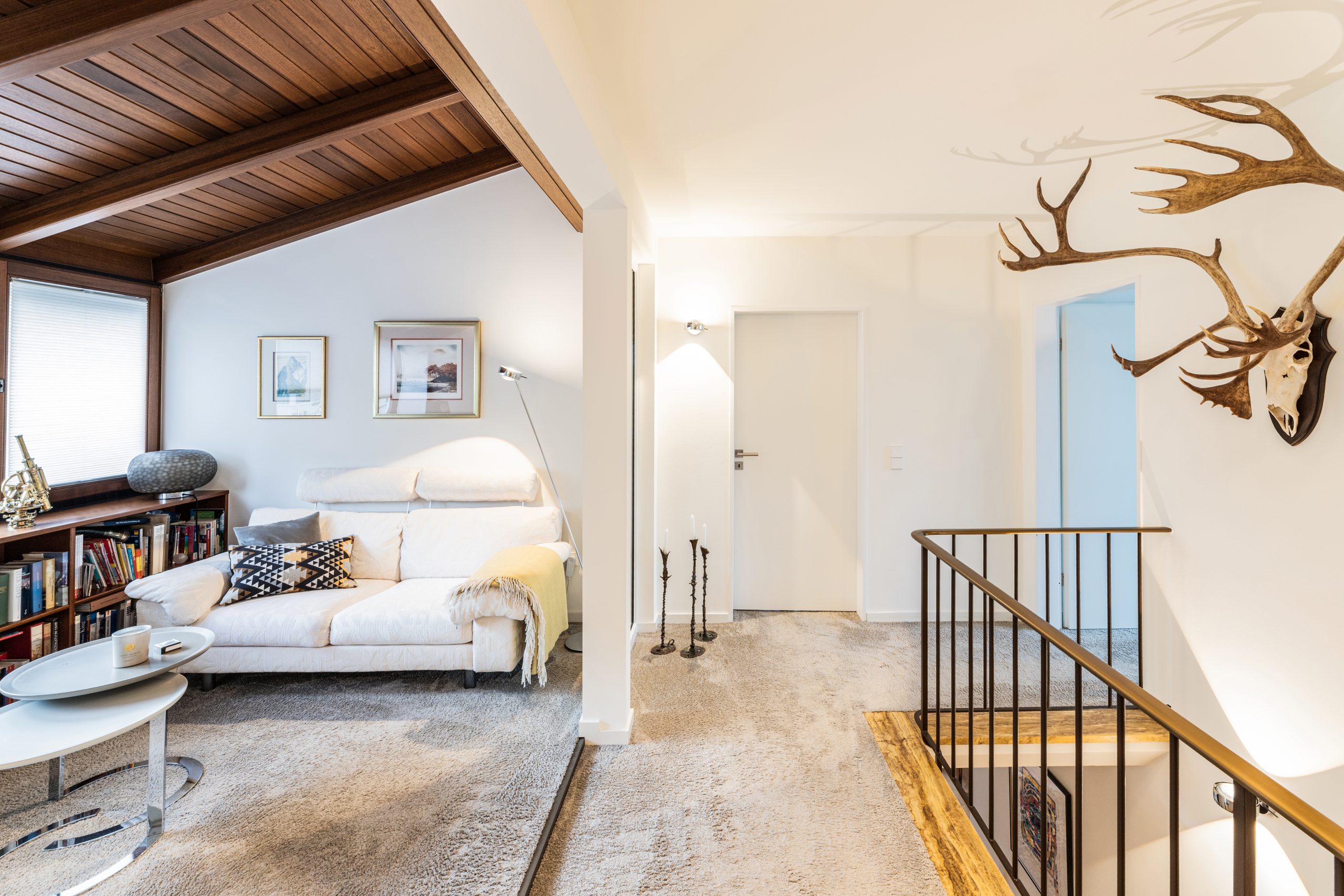 Moderne Lounge mit warmem Licht, Holzdecke, klar weißen Wänden sowie handgefertigten Kunstwerken und Textilien, die eine hochwertige und einladende Atmosphäre schaffen.