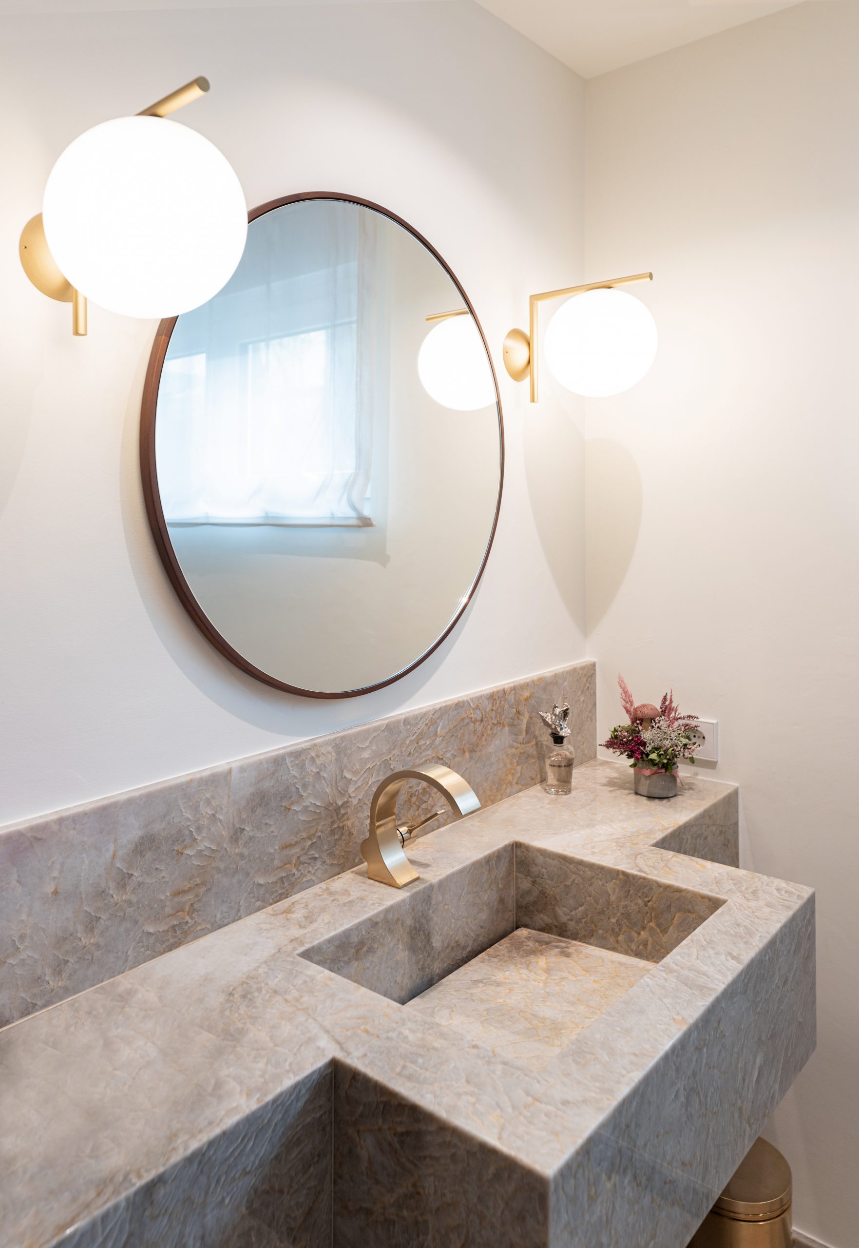 Edler Naturstein mit Tiefe und transparenter Struktur bildet die Grundlage des Designs. Präzise gefertigte Metallarmaturen in hochwertiger Premium-Finish-Ausführung setzen moderne Akzente. Massives Holz und großzügige Designerleuchten ergänzen das Interieur und schaffen eine ruhige, hochwertige Atmosphäre mit klaren Linien und zeitloser Eleganz. michael anastassiades Flos