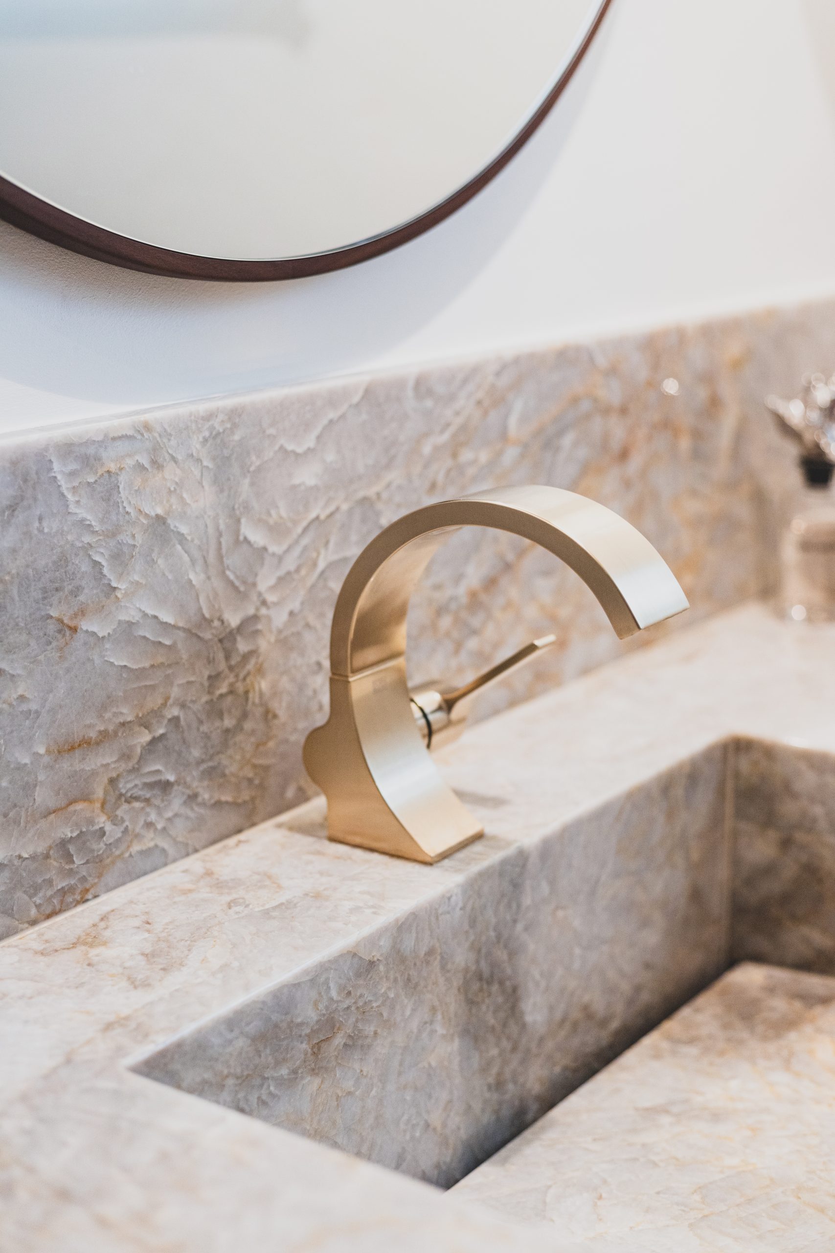 Edler Naturstein mit Tiefe und transparenter Struktur bildet die Grundlage des Designs. Präzise gefertigte Metallarmaturen in hochwertiger Premium-Finish-Ausführung setzen moderne Akzente. Massives Holz und großzügige Designerleuchten ergänzen das Interieur und schaffen eine ruhige, hochwertige Atmosphäre mit klaren Linien und zeitloser Eleganz.